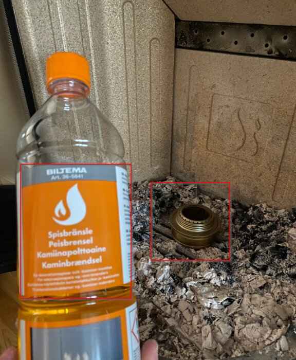 Flaska märkt "Spisbränsle", aska, kamin inre, mässingsskruvlock på askan. Farlig situation, brandrisk.