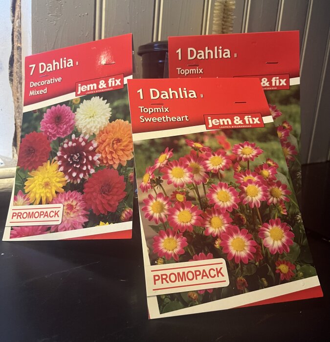 Tre förpackningar med dahliaknölar från jem & fix, olika sorter. Blomsterbilder och text. "PROMOPACK".