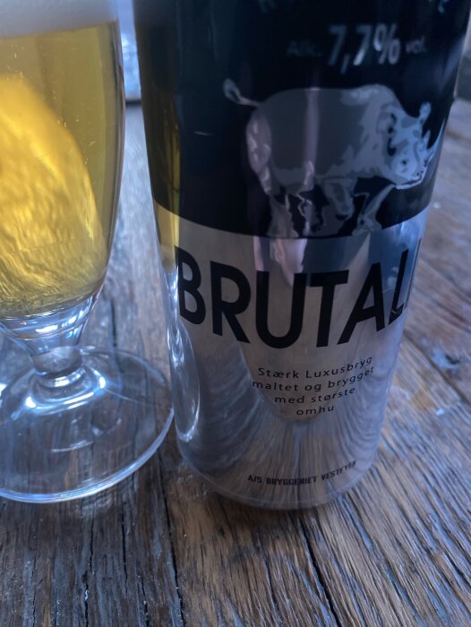 Ölglas och ölburk, text "BRUTAL", alkoholhalt 7,7%, stark luxusöl, träbakgrund.