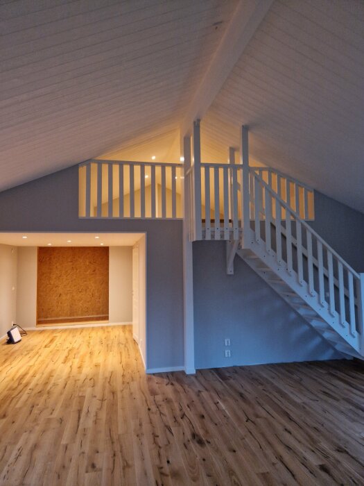 Modernt vindsrum med lutande tak, trägolv, vit trappa och oavslutad vägg eller dörröppning.