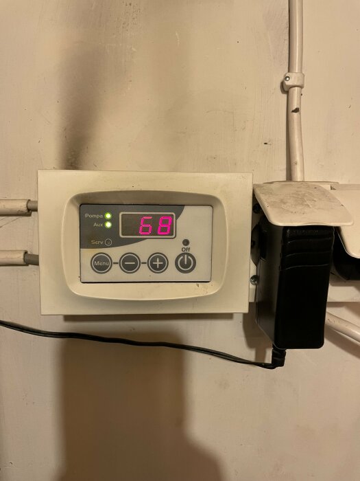 Värmesystem termostat visar 68 grader med gröna indikatorlampor i ett förråd.