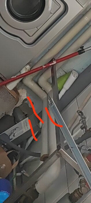 Interiör med VVS-installationer under vask, inklusive rör och ventil, markerat med röda pilar.