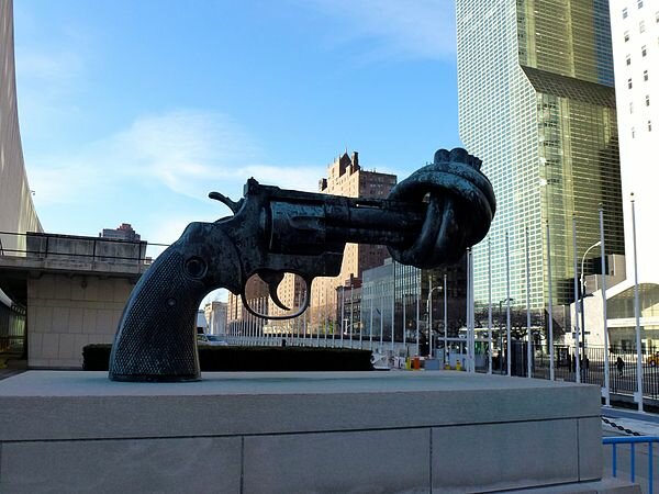 Stor skulptur av en knutlagd pistol som symbol för fred, placerad i en stadsmiljö.