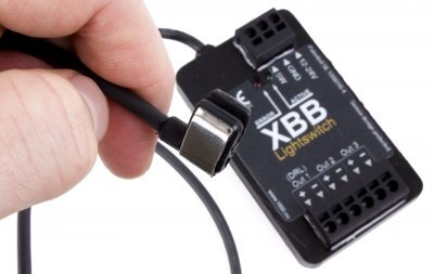 Hand ansluter USB-kabel till elektronisk enhet med text "XBB" på vit bakgrund.