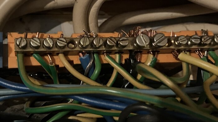 Otydligt foto av en jordskena med anslutna neutralledare och jordledare i en elcentral.