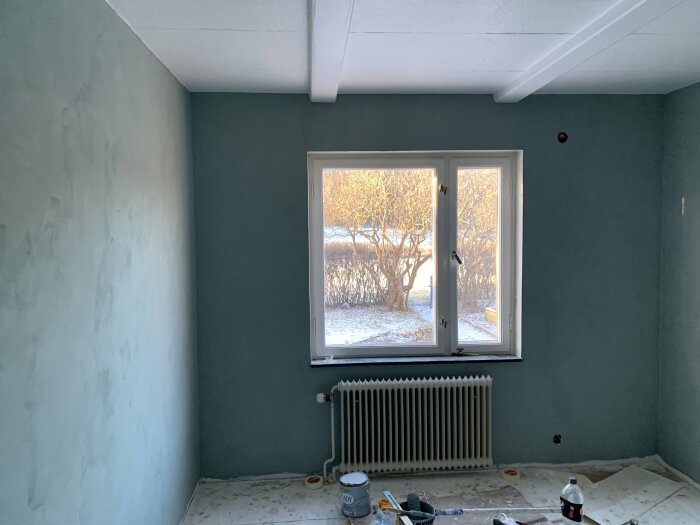 Renoveringsprocess i sovrum med pågående målning med kalkfärg, tomma väggar och målarutrustning.