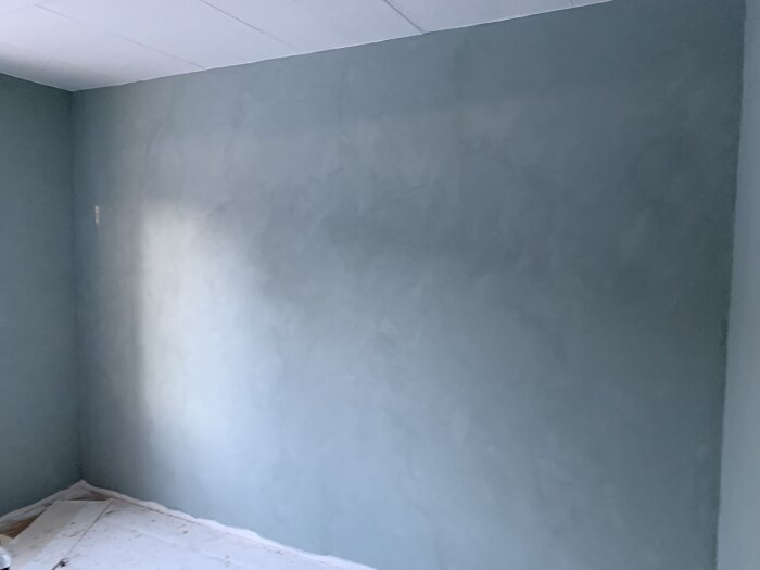 Sovrum med nyapplicerad kalkfärg i blå nyans på väggarna och skyddspapper på golvet.