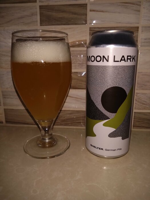 Ölglas fyllt med skummande dryck bredvid en ölburk med texten "MOON LARK".