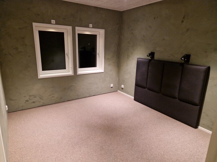 Ett tomt rum med soffa, två fönster och gråa väggar.