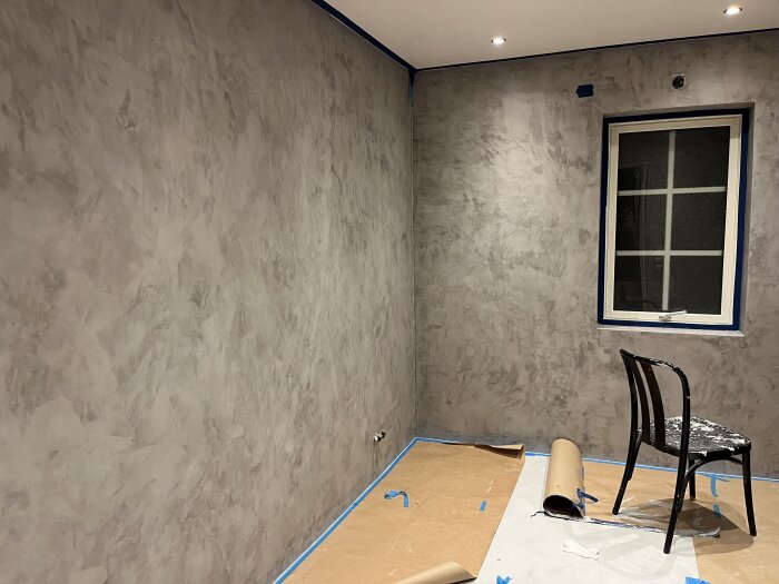 Rum under renovering med en omgång epoxy på väggarna och skyddspapper på golvet.