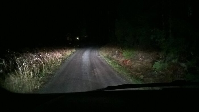 Vy över en mörk landsväg upplyst av halvljuset från en bil, med fokus på ljusstyrkan och fördelningen på vägen.