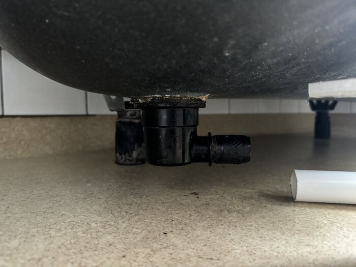 Undersidan av en diskbänk med synliga avloppsrör och kopplingar, behov av reparation syns.
