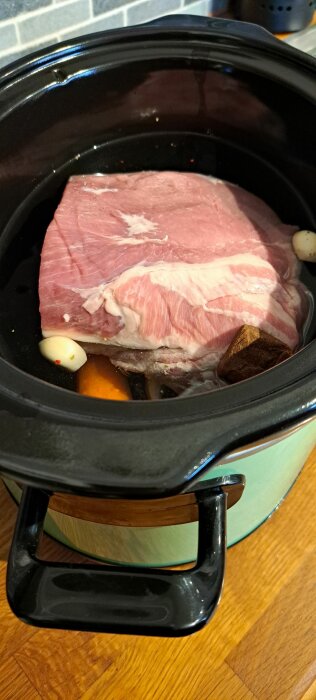 Rå karré i en slow cooker med kryddor och vitlök, förberedelse för carnitas.