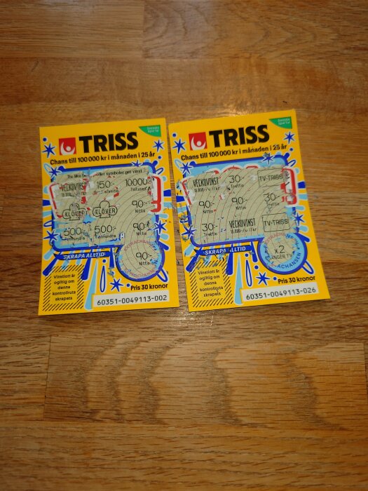Två skrapade Triss-lotter visas på ett träbord, med vinstmarkerade belopp.