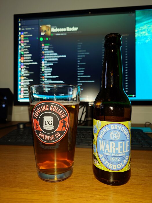 Ett glas öl framför en dator med öppen musiktjänst på skärmen, bredvid en ölflaska från Mora Bryggeri.