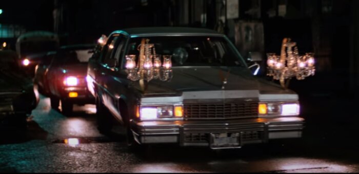 Bild av en Cadillac med ljuskronor monterade på taket, nattetid på en våt gata.