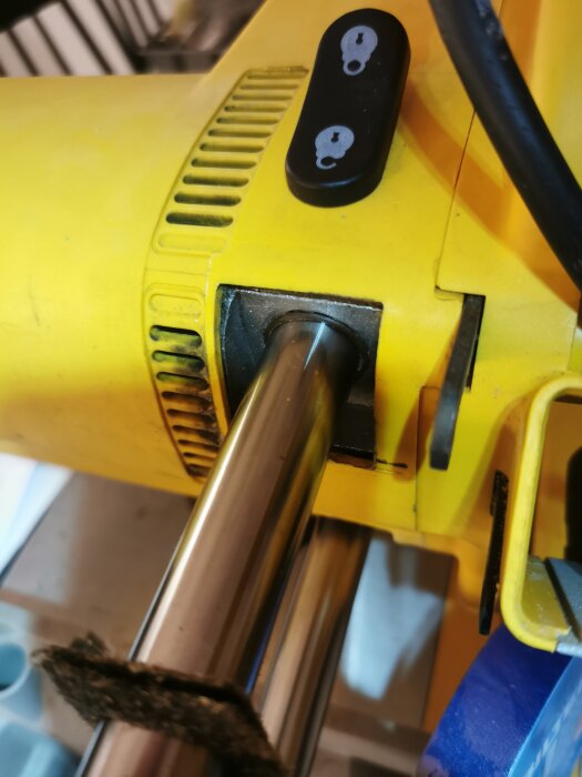 Närbild på gult elverktyg med svart strömbrytare och synlig del av metallstång.