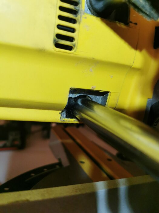 Närgransad bild av en gul maskindel med en svart infästningsklämma och hydraulrör.