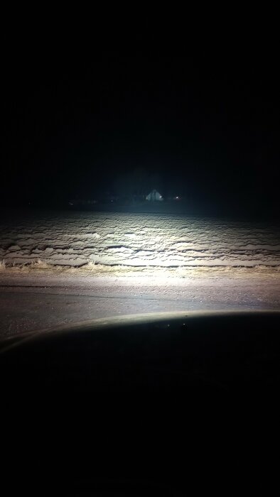 Bild tagen nattetid som visar ett upplyst snötäckt fält med ett hus i bakgrunden.