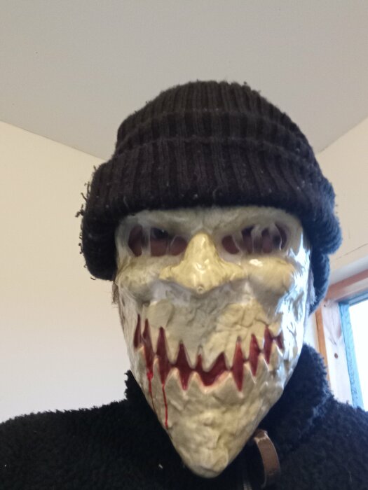 Person med skräckinjagande mask och stickad mössa inomhus.
