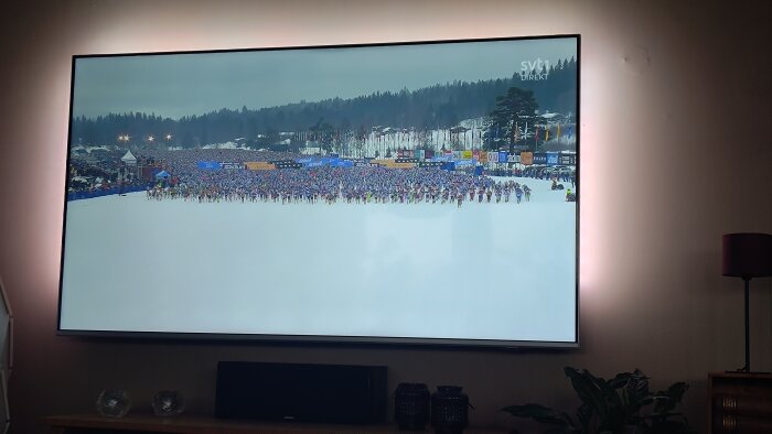 TV-skärm visar en skidtävling med åkare vid startlinjen och publik i bakgrunden.