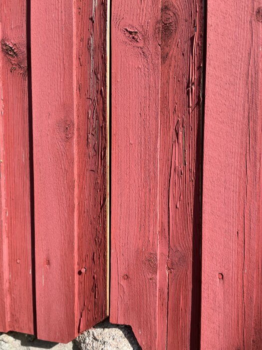 Rödmålat trästaket i solljus med tydlig textur och skuggor.