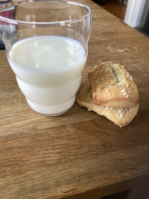 Ett glas mjölk och mandelkubb på ett träbord.