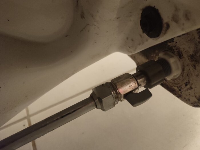 Närbild av en toaletts anslutningsrör med igentäppt litet filter och smuts.