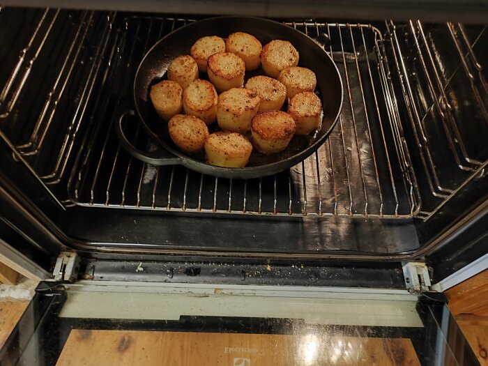 Stekpanna i ugn med brynta, halverade potatisar; matlagning i kök.