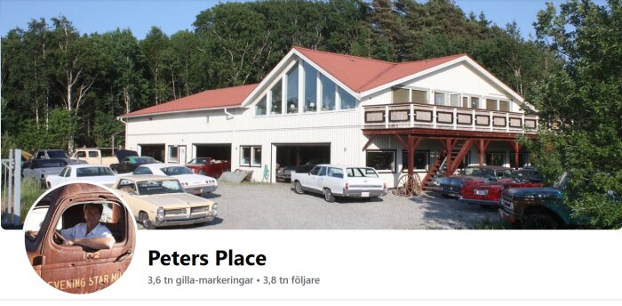 Stort garage med öppna dörrar och samlingshus ovanpå omgivet av klassiska bilar och grönska.