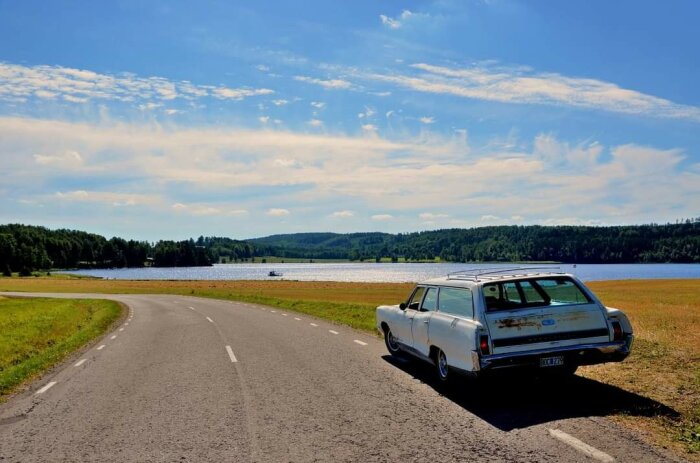 Vit '66 Bonneville station wagon parkerad vid en landsväg med sjö och skog i bakgrunden.