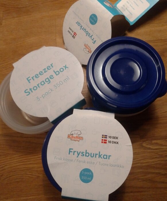 Runda plastburkar märkta "Freezer Storage box" och "Frysburkar", några med blå lock, förpackade och upplagda på ett bord.