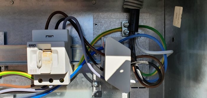 Elektrisk kabelanslutning med säkring, kopplingslåda och ledningar i ett elskåp.
