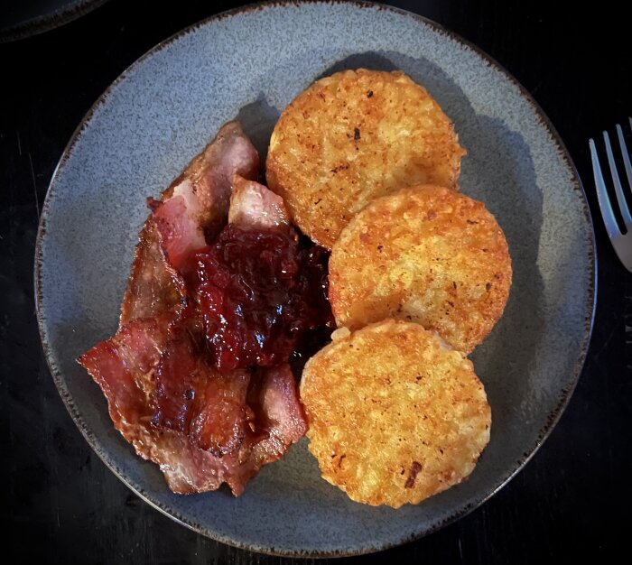 En tallrik med stekt bacon, lingonsylt och rostade potatiskakor.