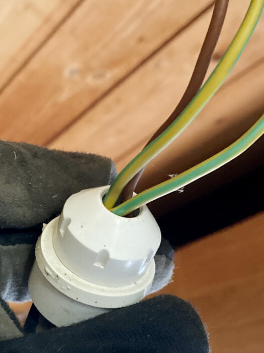 Närbild av en elektrisk installation med en vit toppklämma och färgade kablar mot träbakgrund.