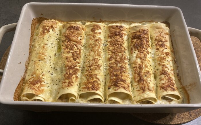 Ett ugnsform med gyllenbruna cannelloni fyllda med ricotta och spenat, toppade med ost och örter.