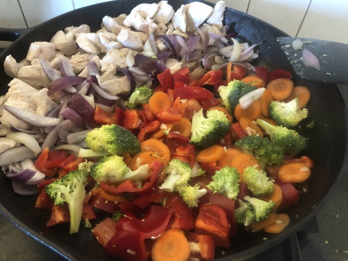 Wok med kyckling, röd paprika, morot, broccoli och rödlök på spisen.