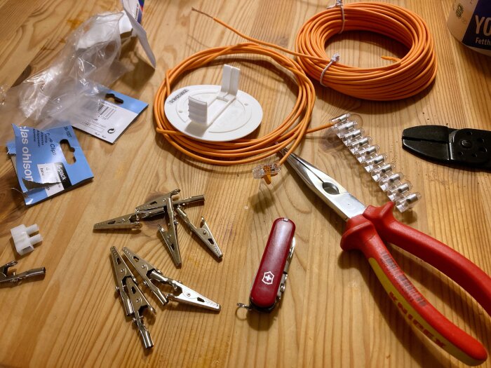 Elektronikkomponenter på ett bord: krokodilklämmor, orange kabel, pluggar, skarvdon och verktyg.