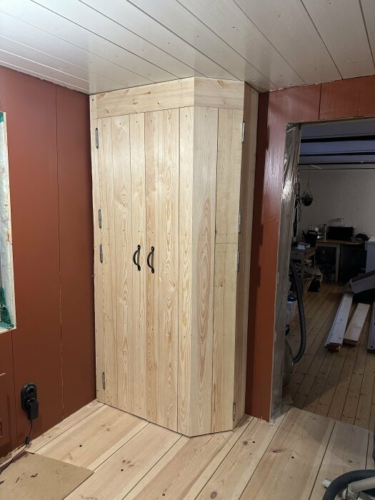 Trähörnskåp i ett rum under renovering, synliga verktyg och byggmaterial, blandad inredningsdesign, obehandlat trä.