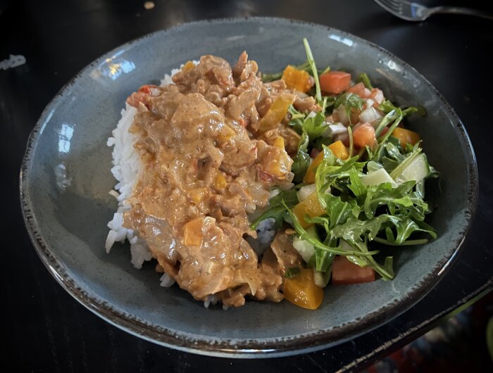 En tallrik med ris, krämig sås, tärnad paprika och en sallad med ruccola, tomat och ost.