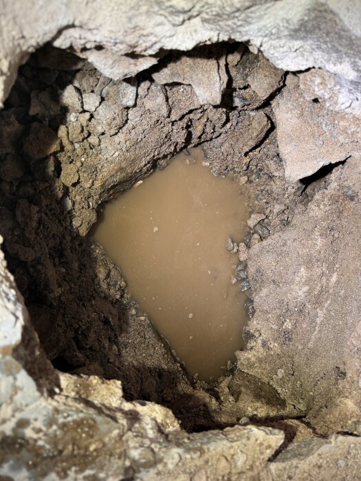 Ett hål i jorden med sprickor och brunaktigt vatten. Möjligtvis en brunn eller erosionsproblem.