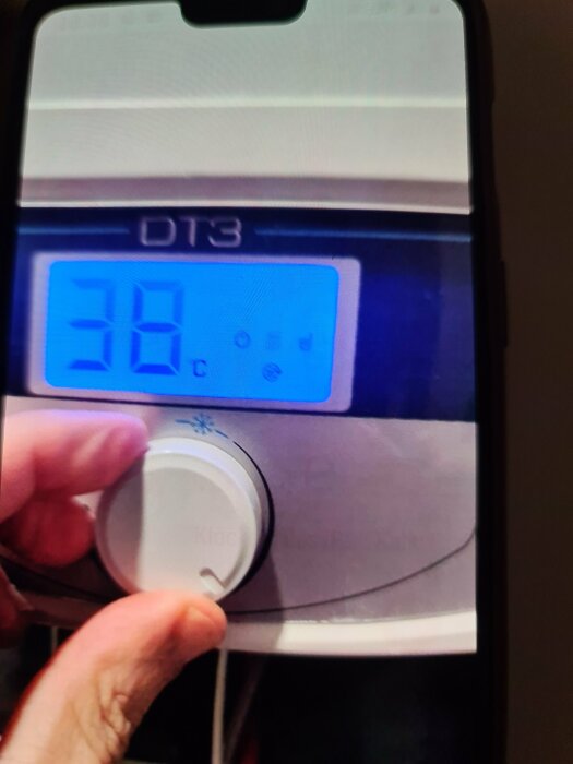 Person justerar digital termostat på varmvattenberedare visande 38 grader Celsius.