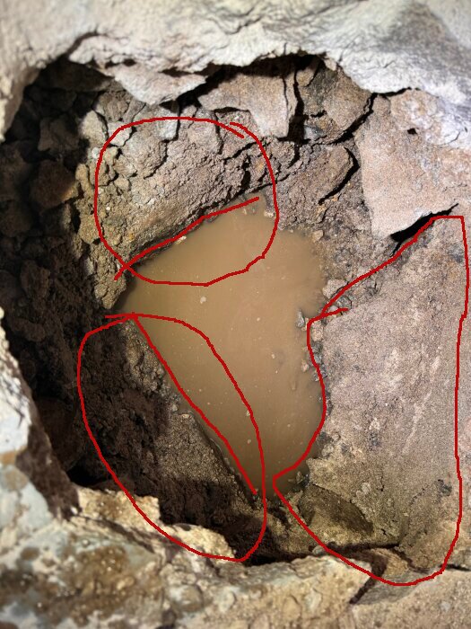 Gjuten struktur synlig i en grop under ett golv med vattenansamling, omgiven av röd markering.