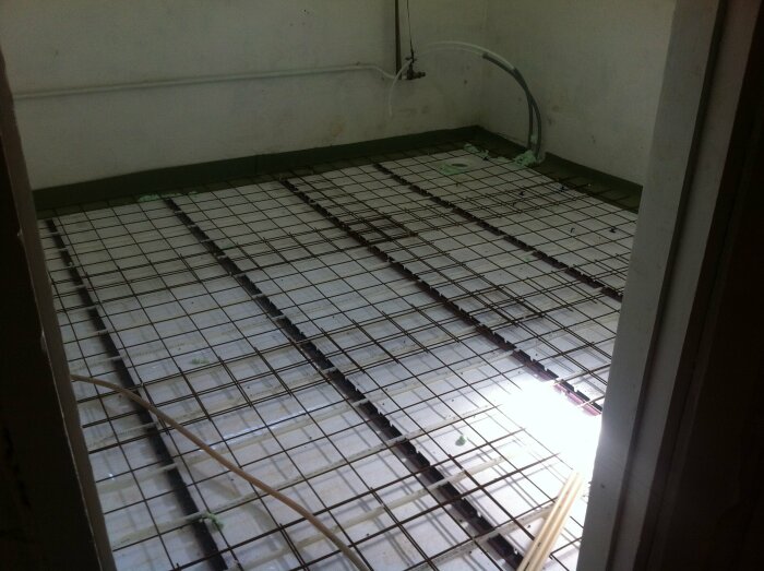 Installation av golvvärme med nätmattor och rör före betonggjutning i ett rum under renovering.
