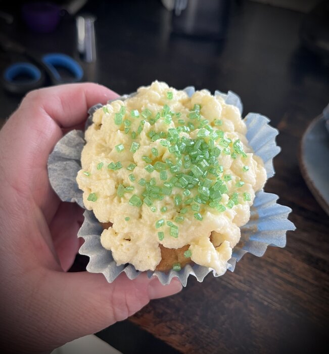 Hållen cupcake med klick gräddig frostning och strössel av gröna kristaller, serverad på blått form.