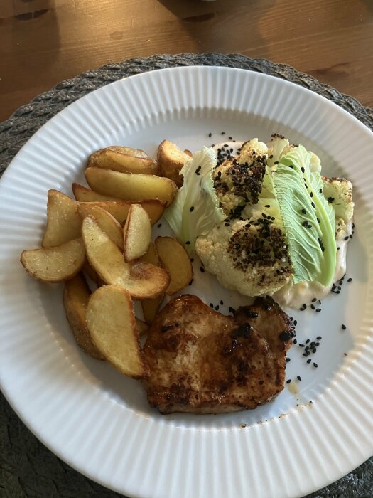 Marinerad fläskhare, potatisklyftor, blomkål med dressing och blad, svarta sesamfrön på vit tallrik.