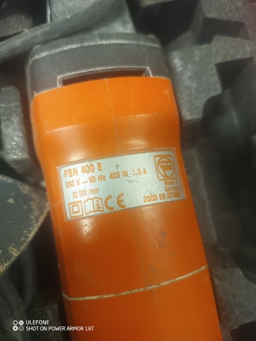 Verktyg med teknisk etikett: FSN 400 E, orange, metall, 400 W, delvis synlig grå plast, suddig bakgrund.