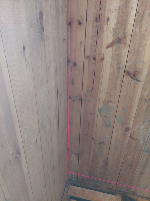 En vägg av träbrädor med en rosa lasernivålinje som visar att väggen lutar något från golvet till taket.