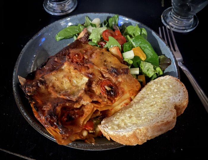 En portion tonfisklasagne arrabiata med sallad och ett stycke vitlöksbröd på en tallrik.