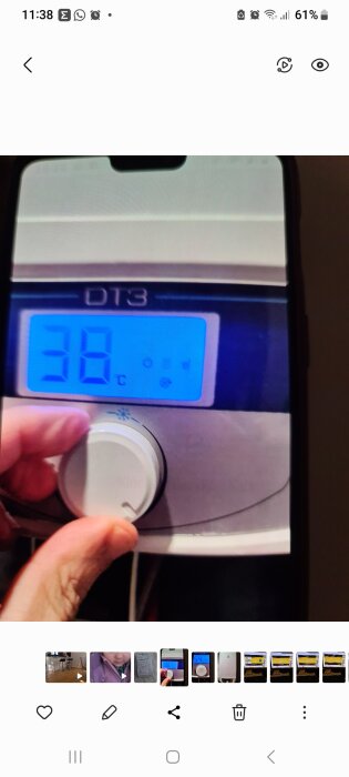 En hand håller en mobil som visar en bild på ett termometer som indikerar 30 grader Celsius.